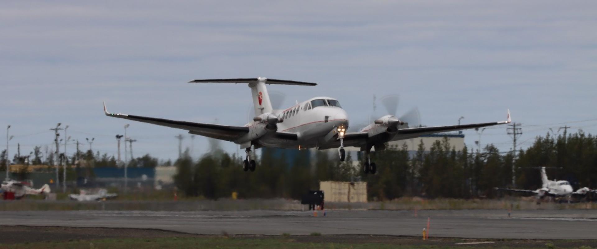  AI Generated Alt Text The image features a small white airplane flying low over a runway.