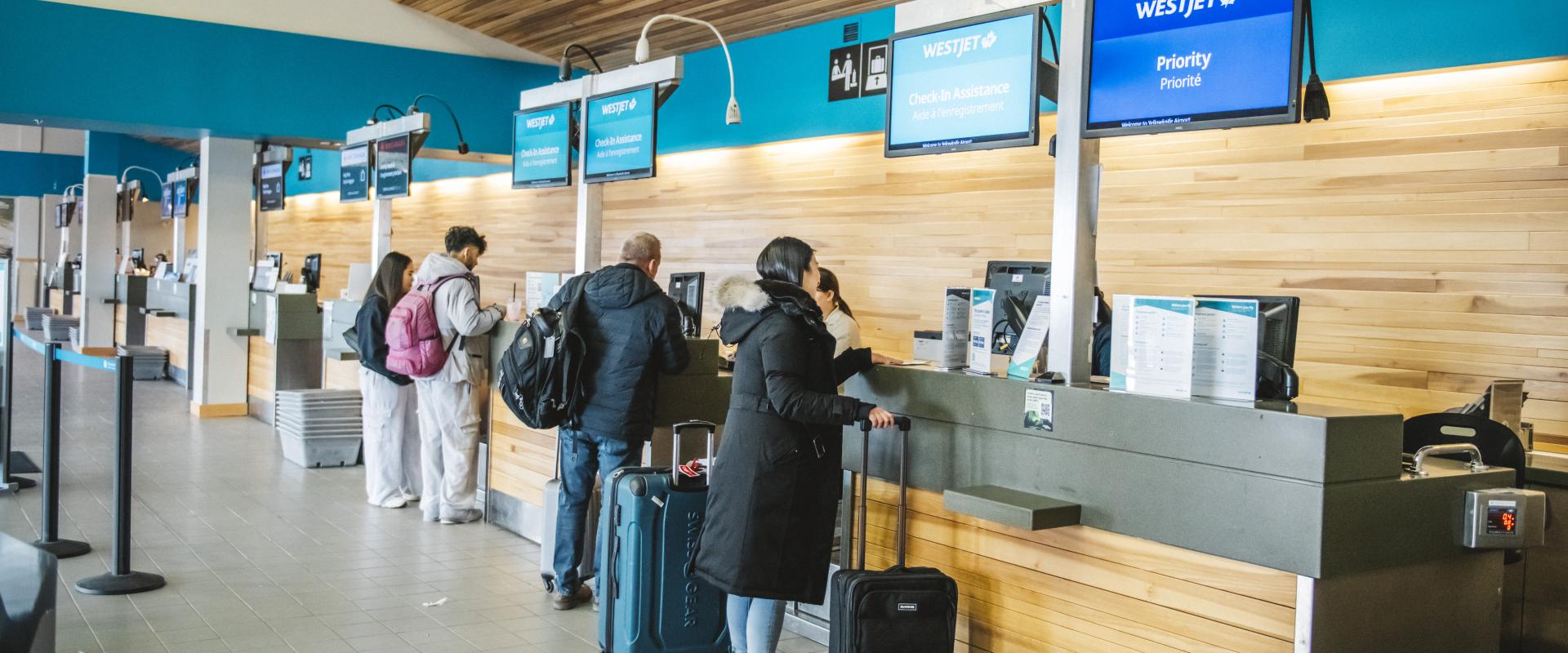 The image depicts a busy airport scene with several people standing in line at a check-in counter.